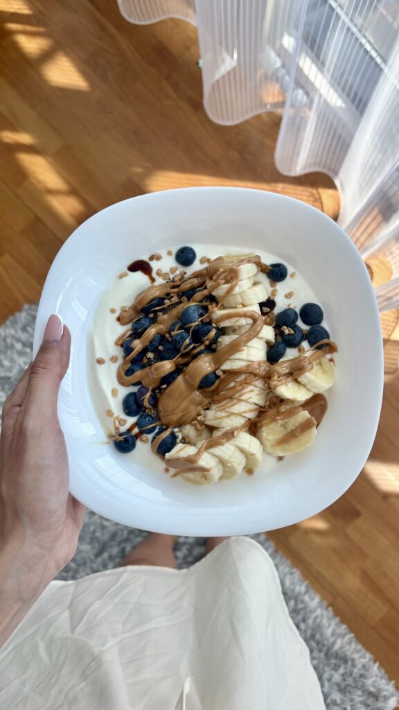 yogurt bowl with sliced bananas, blueberries, and peanut butter drizzle in a white bowl